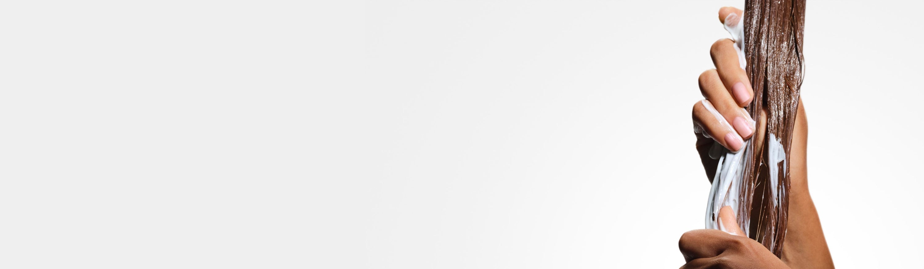 Hands running OLAPLEX No.3PLUS Complete Repair Treatment through brown hair strands 