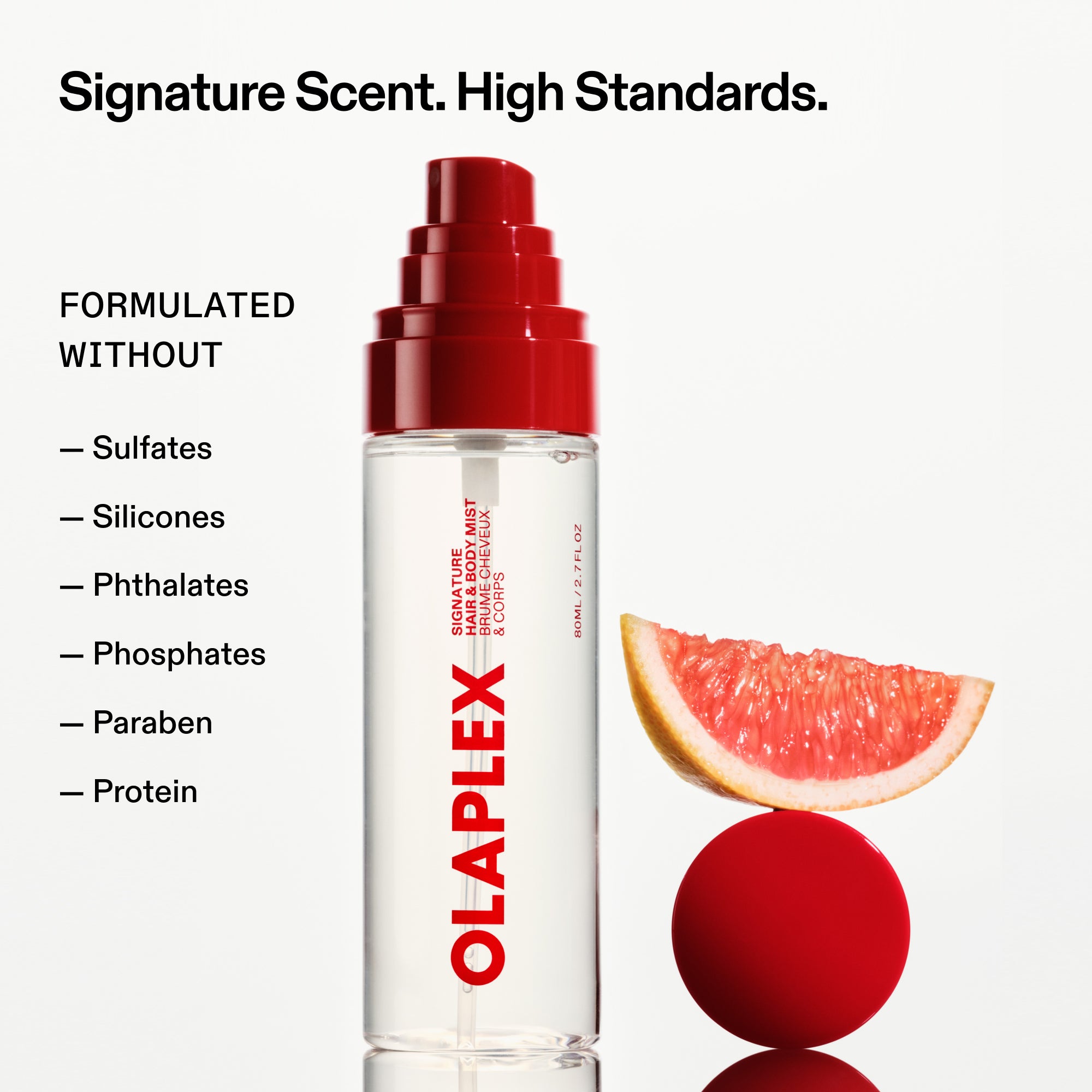 An OLAPLEX hair and body mist bottle stands next to a grapefruit slice balanced on a red sphere. Text at the top reads, "Signature Scent. High Standards." A checklist on the left reads, "FORMULATED WITHOUT: Sulfates, Silicones, Phthalates, Phosphates, Paraben, Protein.