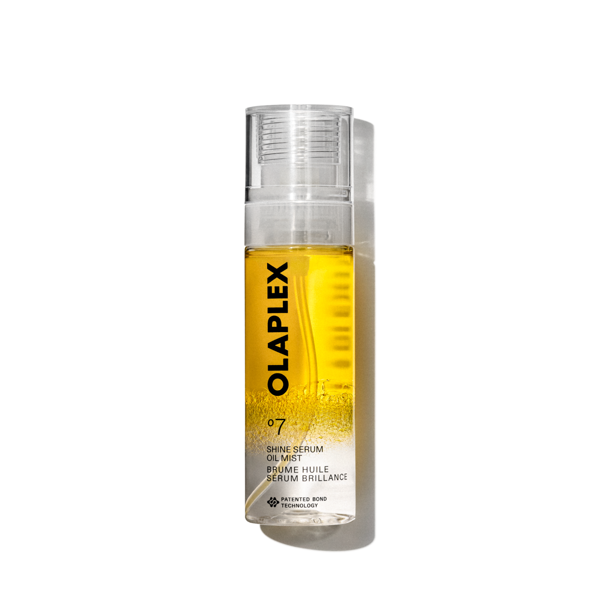 A product packshot of Olaplex No. 7 Shine Serum Oil Mist in an 80ml clear spray bottle. The bottle features a bright yellow liquid visible inside, a transparent cap, and a clean white label at the bottom with black text displaying the product name, details, and the signature "No. 7" logo. The bottle is isolated against a transparent grid background.